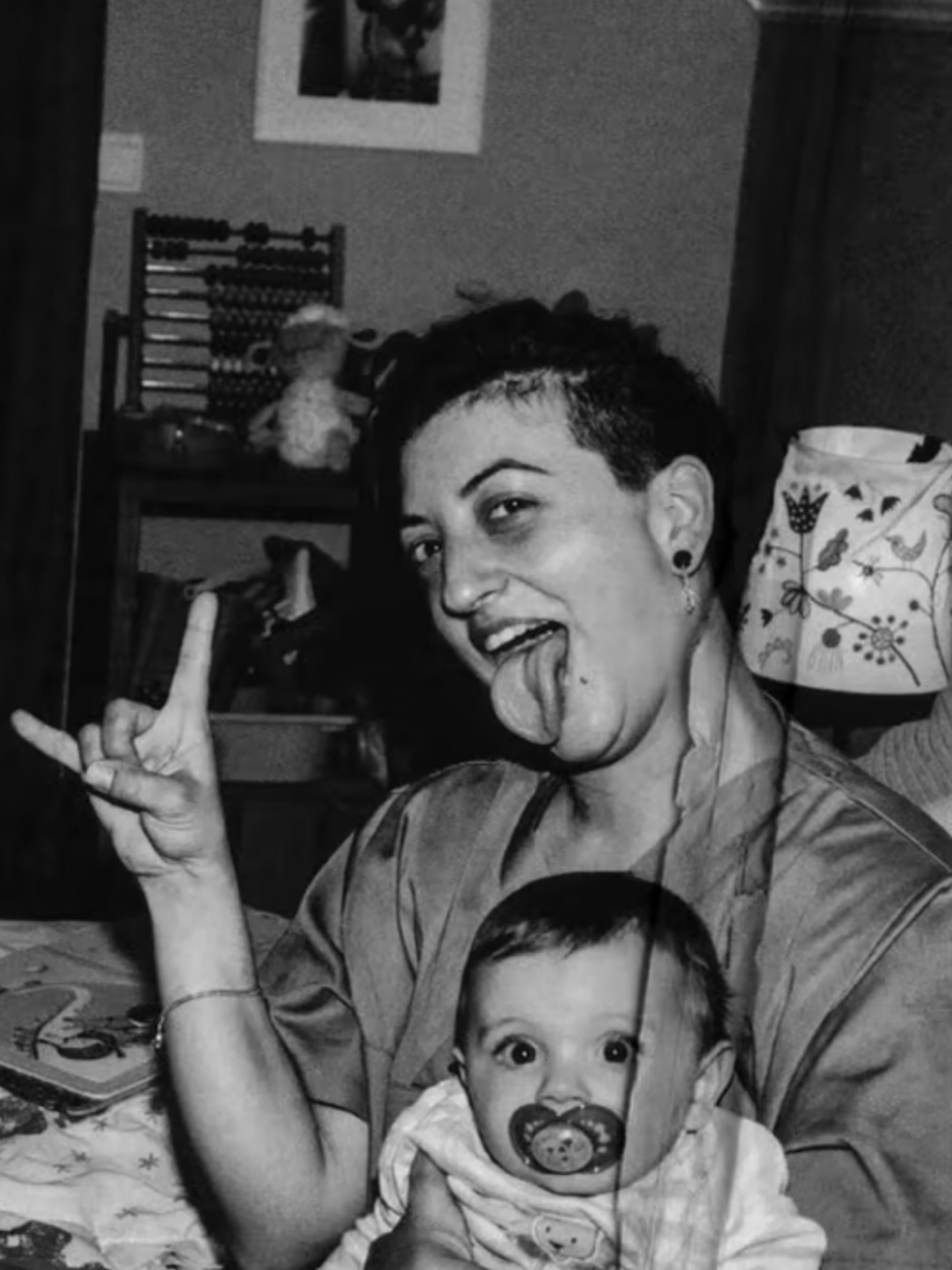 Mother making a rock sign holding a baby on a bed