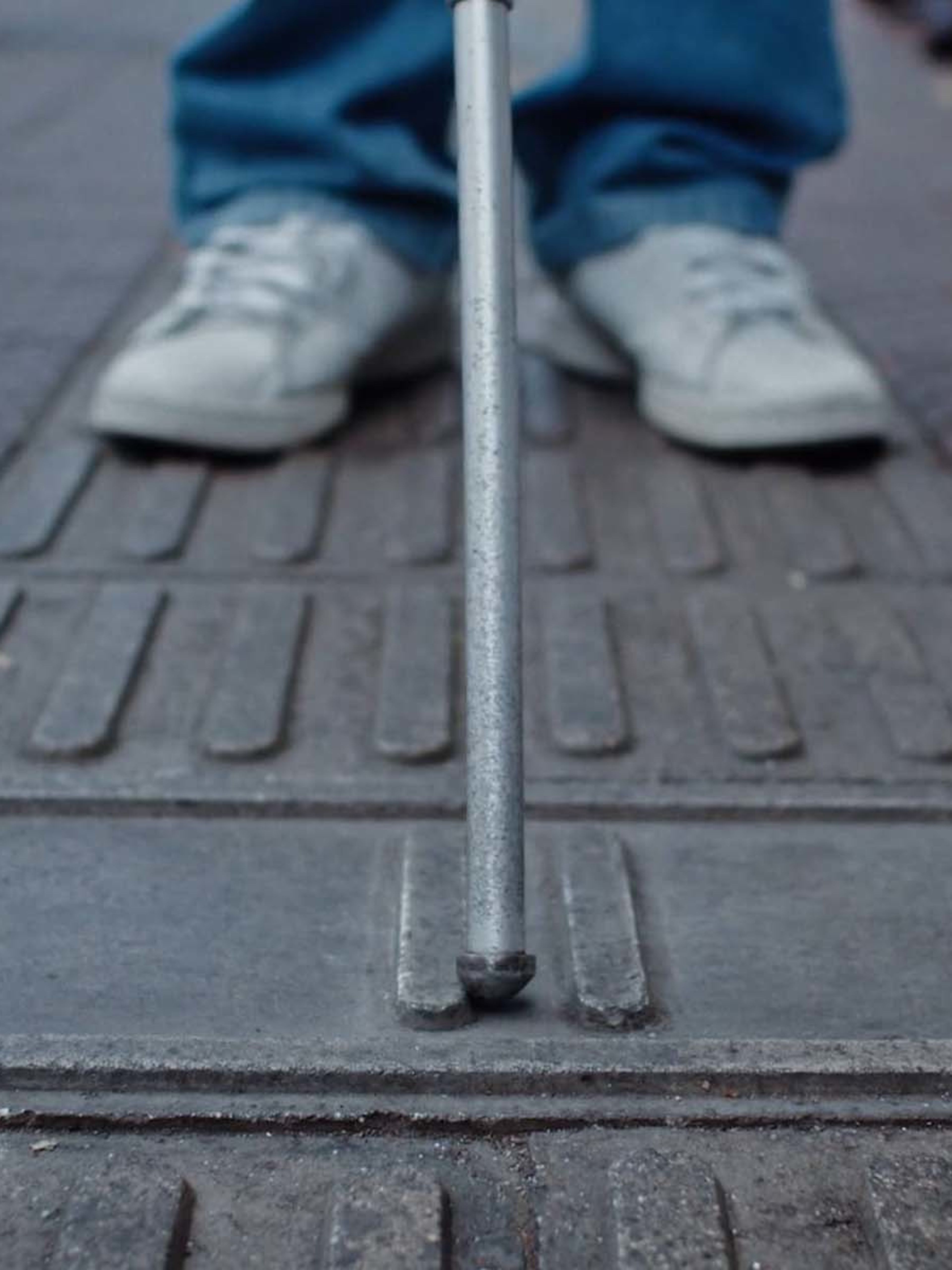 Ground level shot of a person with a walking stick for blind and partially sighted people using the pavement pattern developed by Cemento Sol to establish where they are on the street