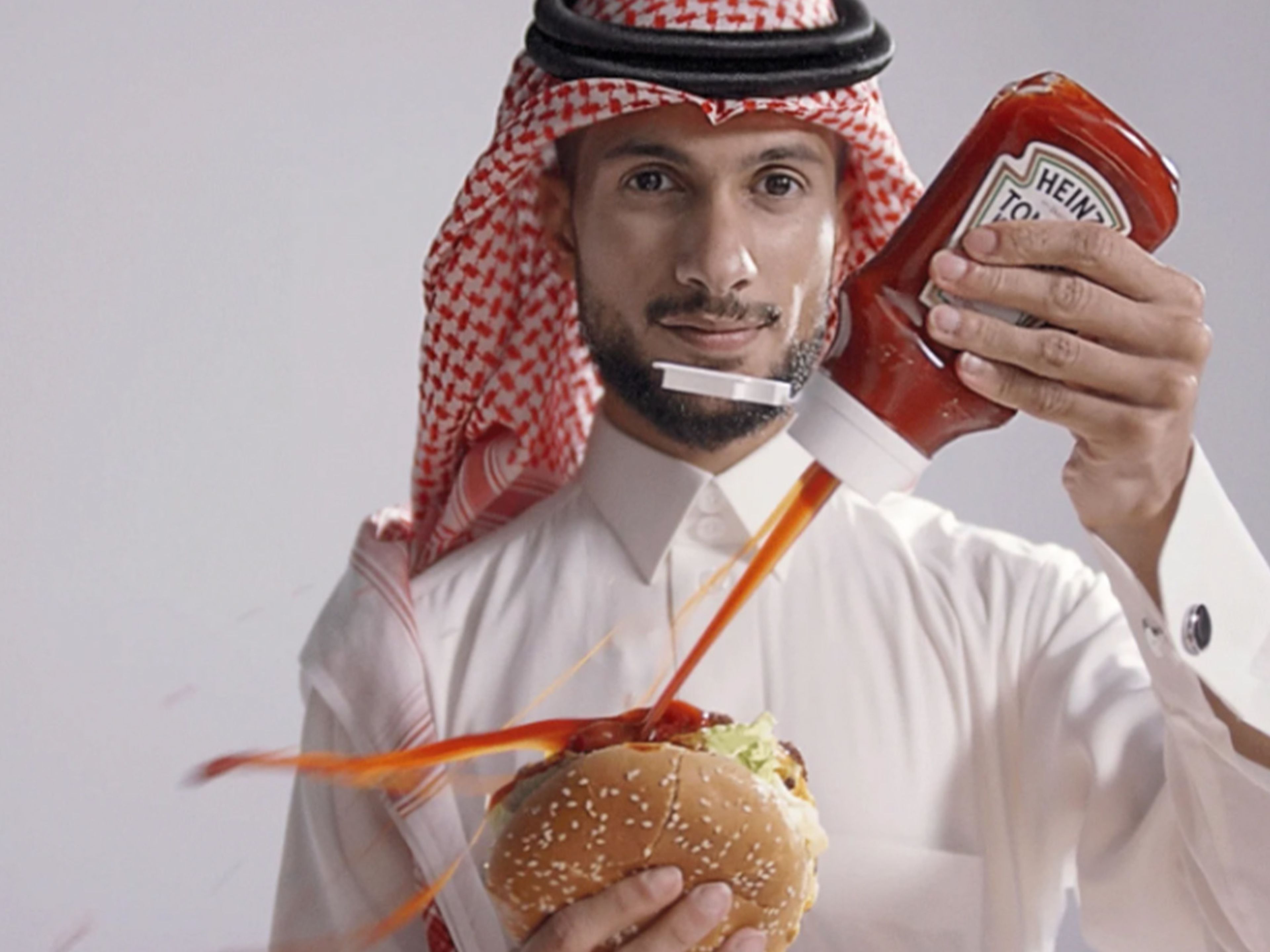 Man dressed in a thobe squirting Ketchup onto a burger