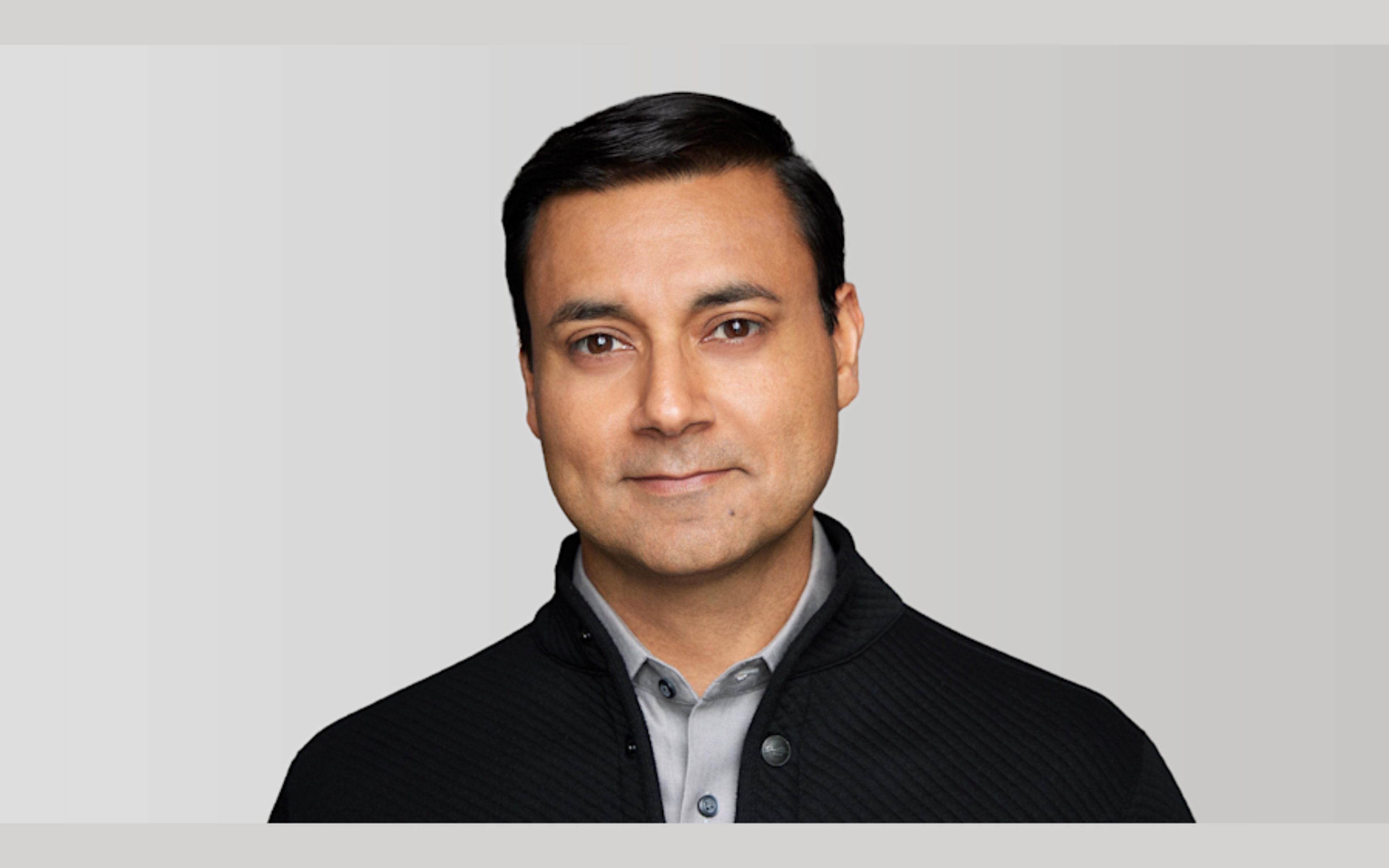 Professional headshot of a man in a black cardigan and blue shirt
