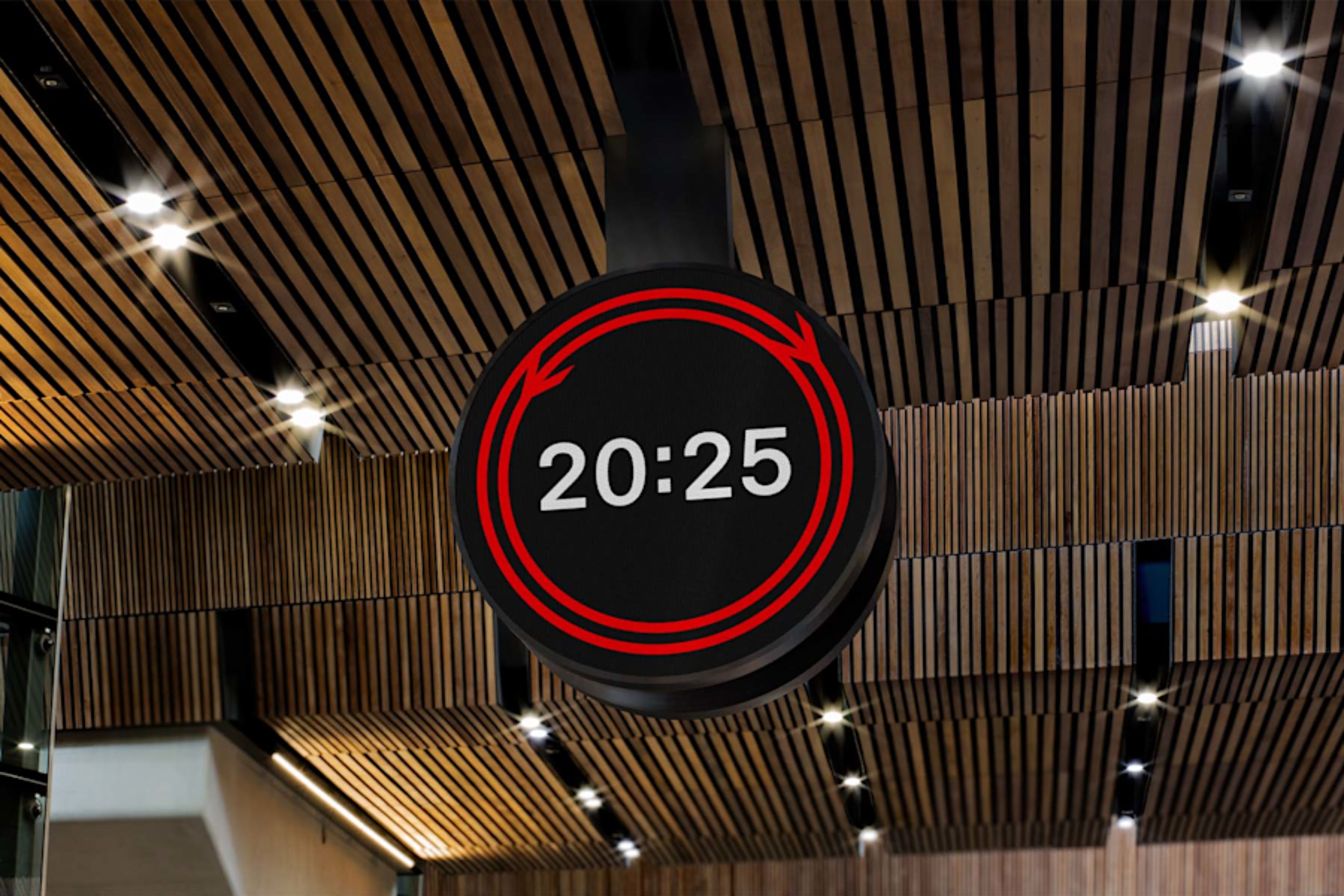 A black circular sign displaying '20:25' in white text, surrounded by red circular arrows, hangs from a modern wooden slatted ceiling with spotlights