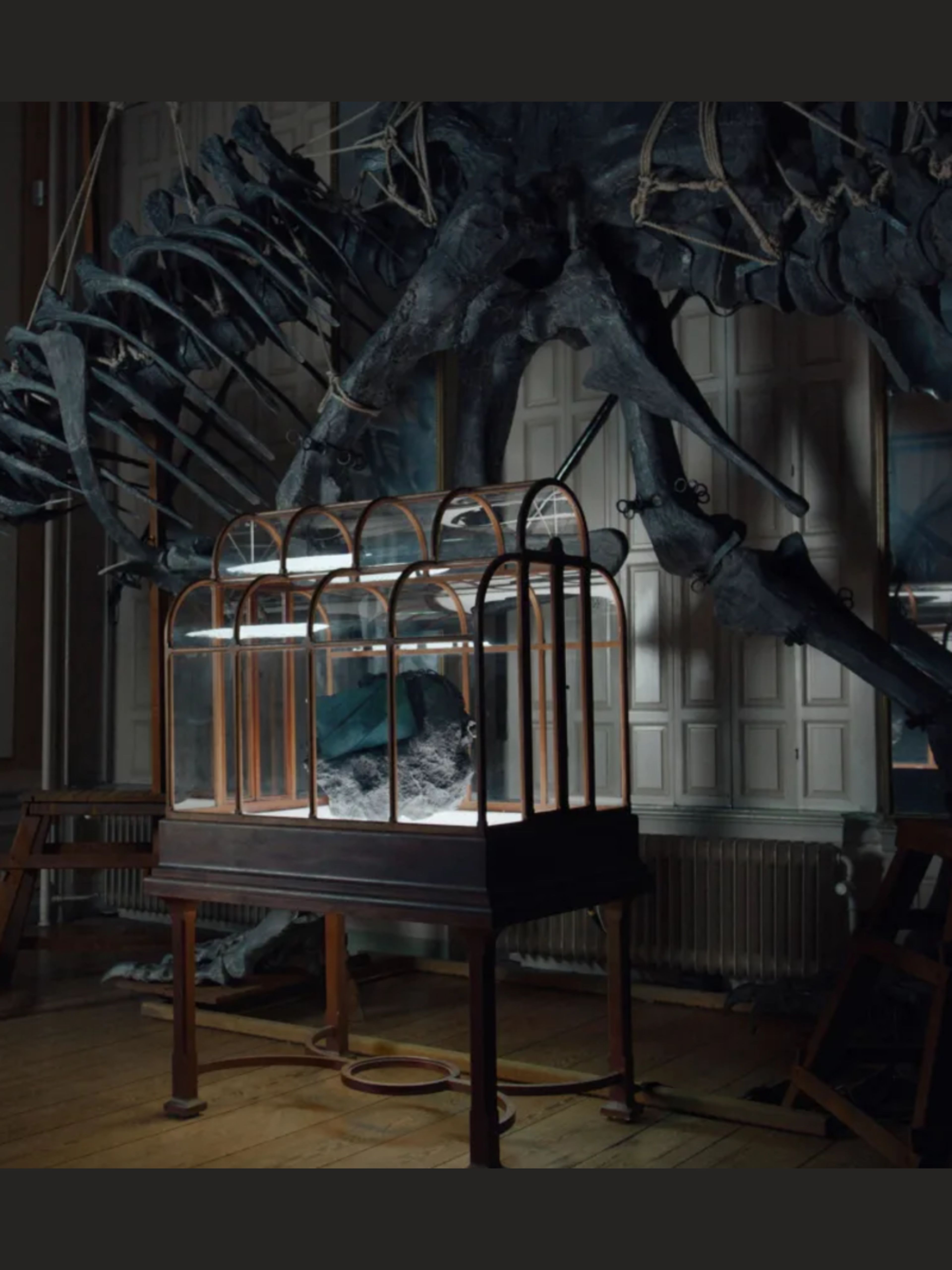 Dinosaur skeletons suspended above an iron bed in shadowy room