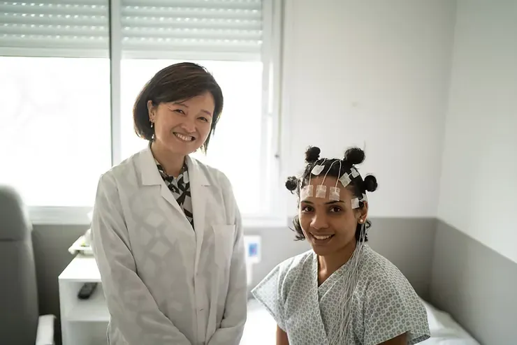 Profissional de saúde ao lado de uma paciente com eletrodos posicionados na cabeça para um EEG.