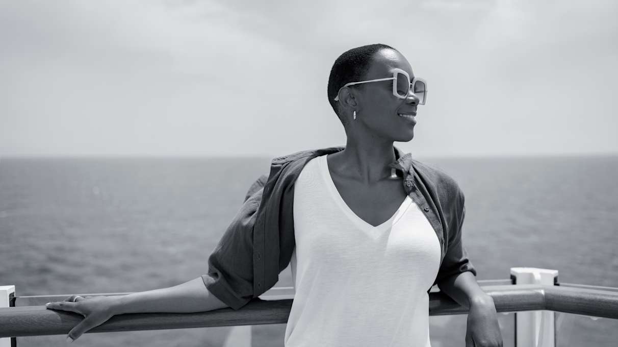Black & white image of a solo womn looking out to sea on deck of a Cunard ship