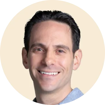 smiling man with short dark hair wearing a light blue shirt, neutral background with circular crop around the face