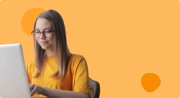 young woman in a yellow shirt using a laptop on an orange background, casual workspace scene with bright colors