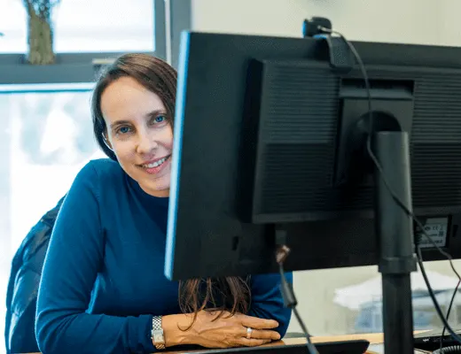 smiling woman working at a computer desk, office environment with natural light and modern technology