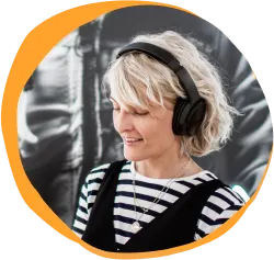 woman with headphones smiling, striped shirt and short blonde hair against a vibrant background