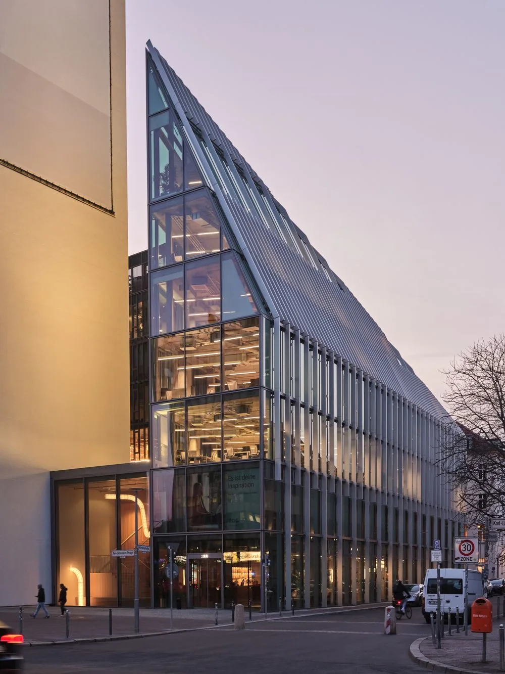 modern glass building with angular design and urban setting, evening light illuminating the structure, urban architecture glass facade