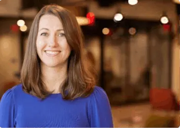 smiling woman in blue top with long hair in modern workspace, professional setting with soft lighting and blurred background