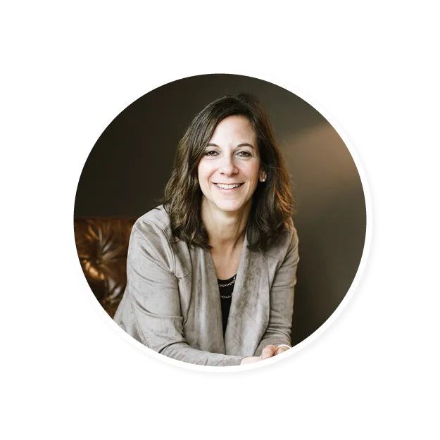 woman smiling in a circular frame, wearing a gray blazer, seated, warm lighting, relaxed atmosphere, professional portrait of a woman with brown hair, casual setting, inviting smile