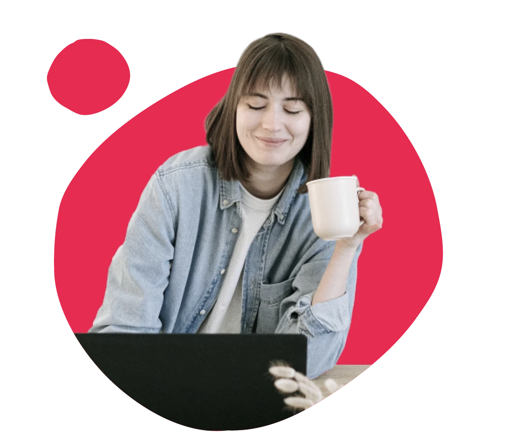 smiling woman in denim shirt holding a coffee cup while working on a laptop against a vibrant red background, remote work lifestyle