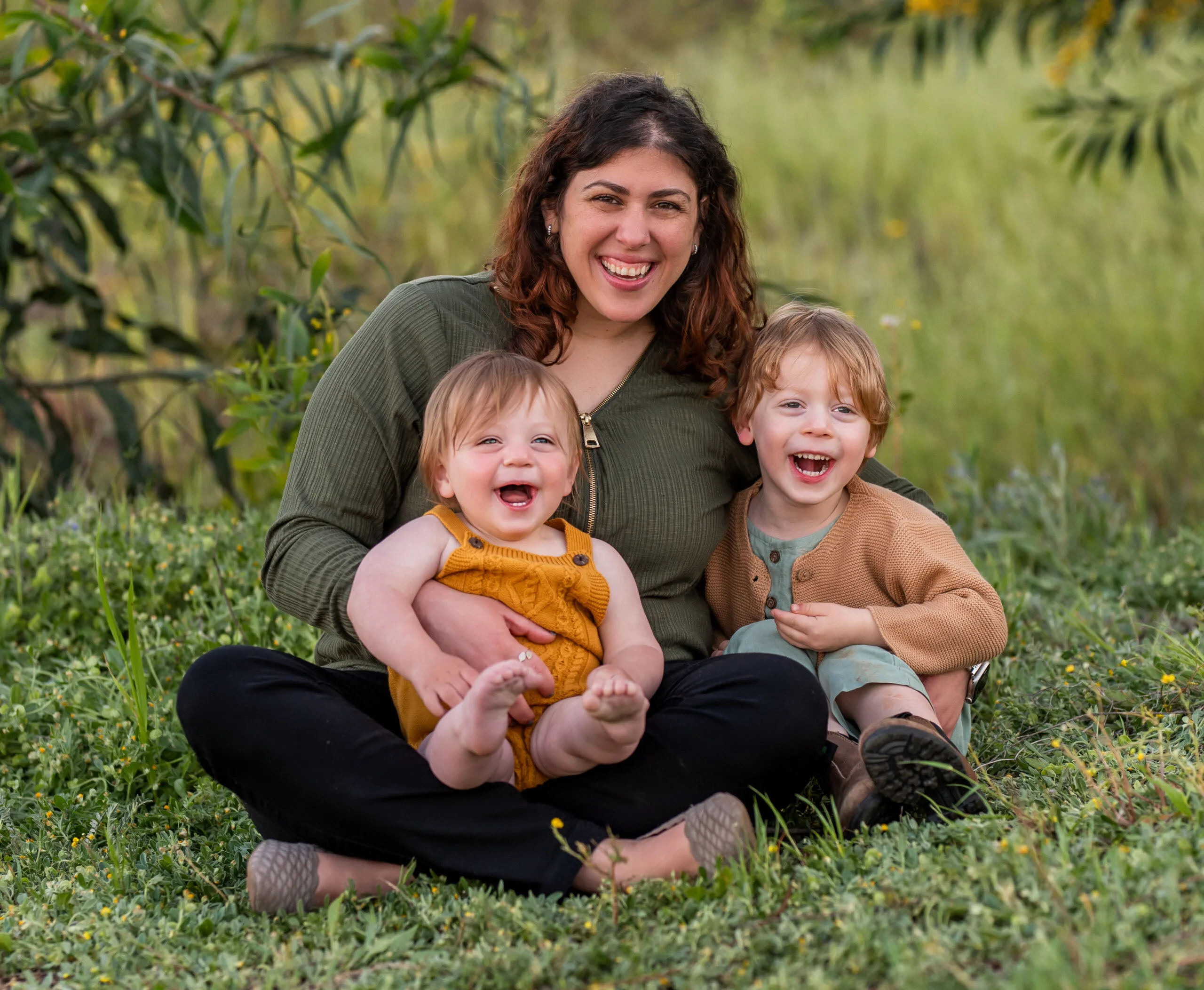 mother with two children sitting on grass, smiling happily in a natural setting, family portrait with kids outdoors