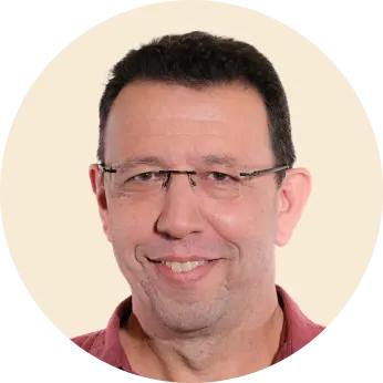 smiling man with glasses in a circular frame, casual portrait with neutral background and warm expression