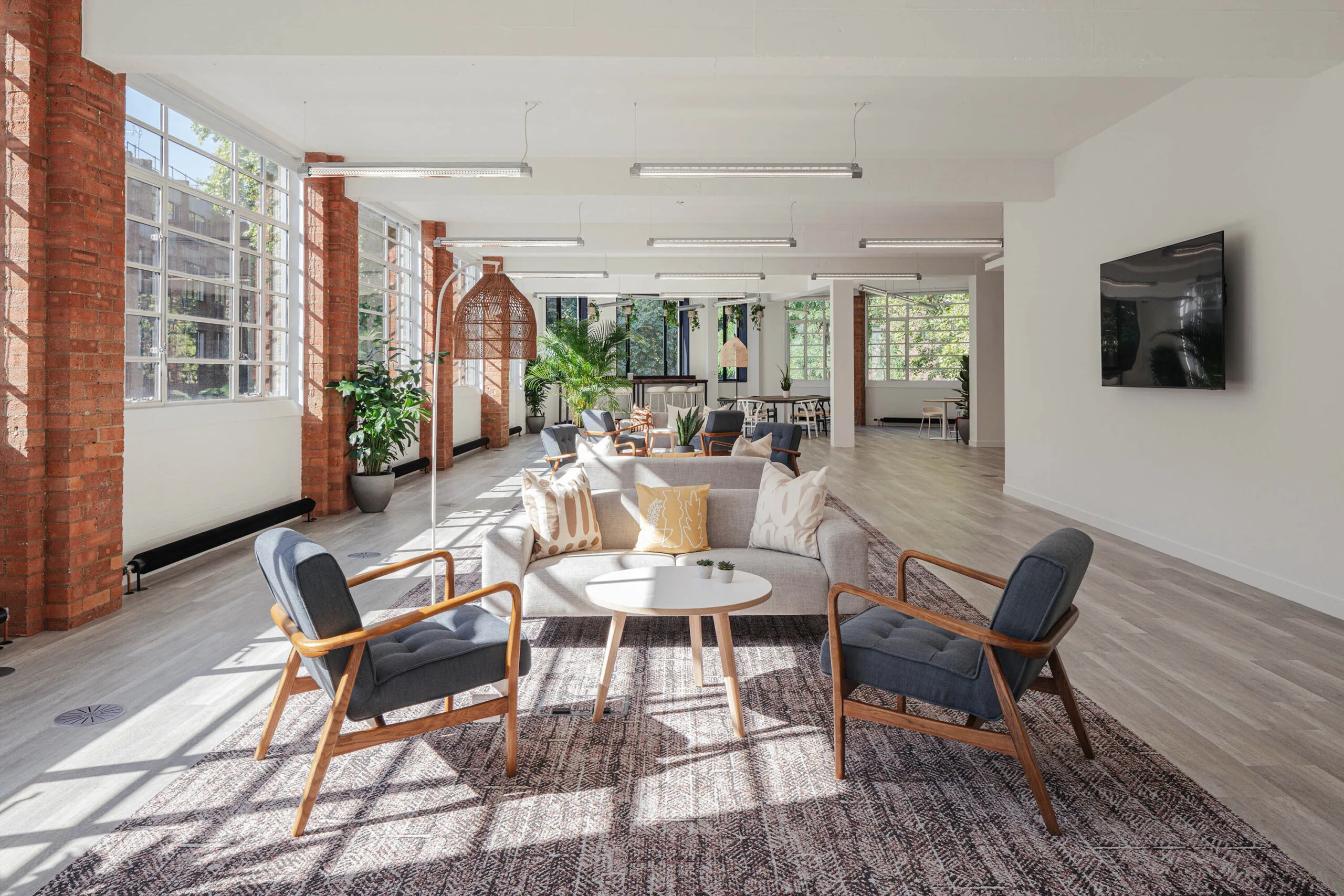 modern open-concept lounge with large windows, cozy seating, wooden accents, and greenery, bright airy space featuring stylish decor and natural light