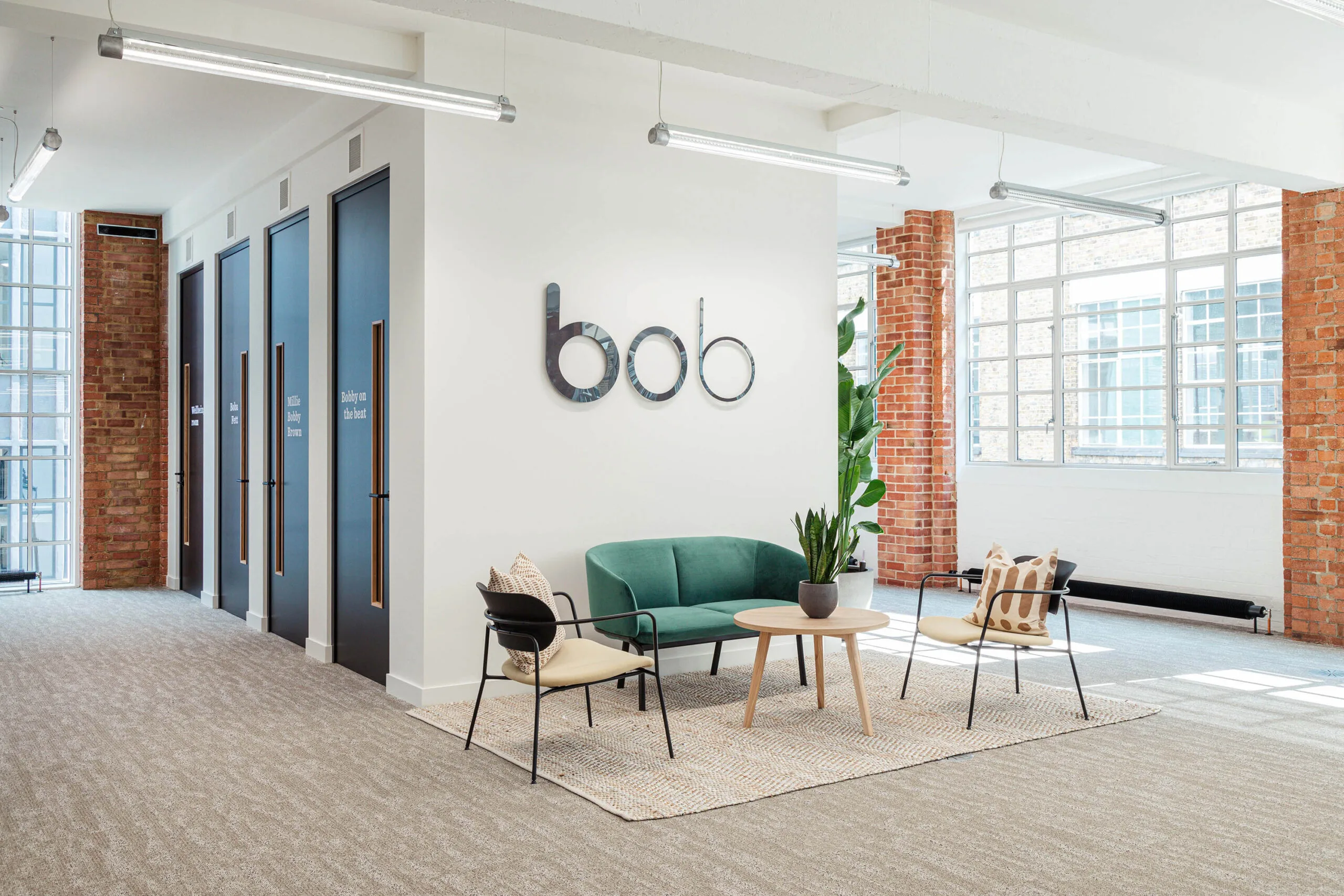 modern office lobby with green sofa, wooden table, and natural light; stylish decor and vibrant brick walls, contemporary workspace featuring seating area and meeting rooms