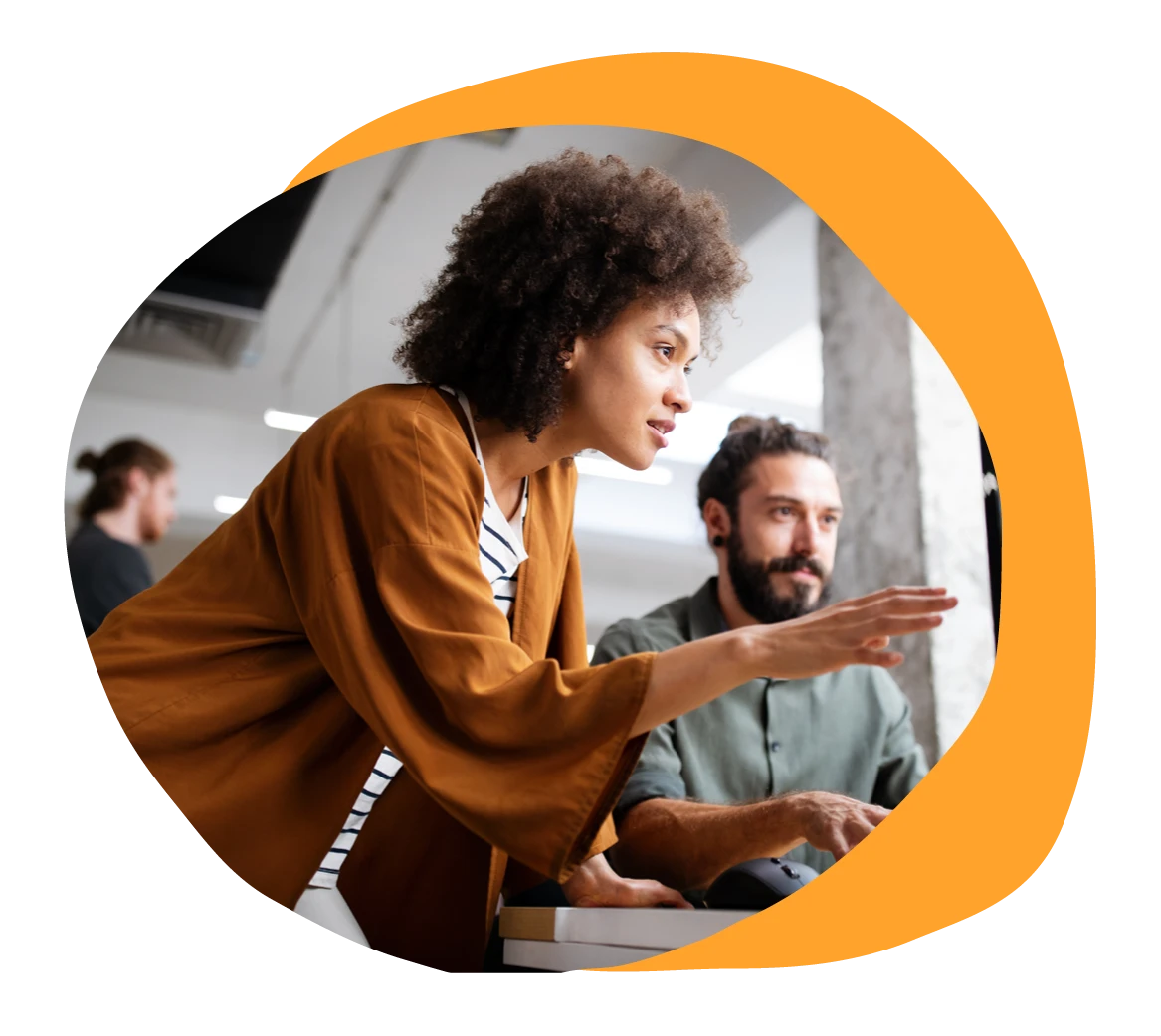 collaborative workspace with two coworkers discussing a project, one gesturing towards the screen, modern office setting, teamwork in an office, engaging discussion between colleagues, focused expressions