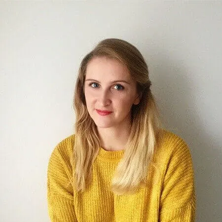 young woman in bright yellow sweater with long blonde hair against a plain light background, cheerful portrait with natural light