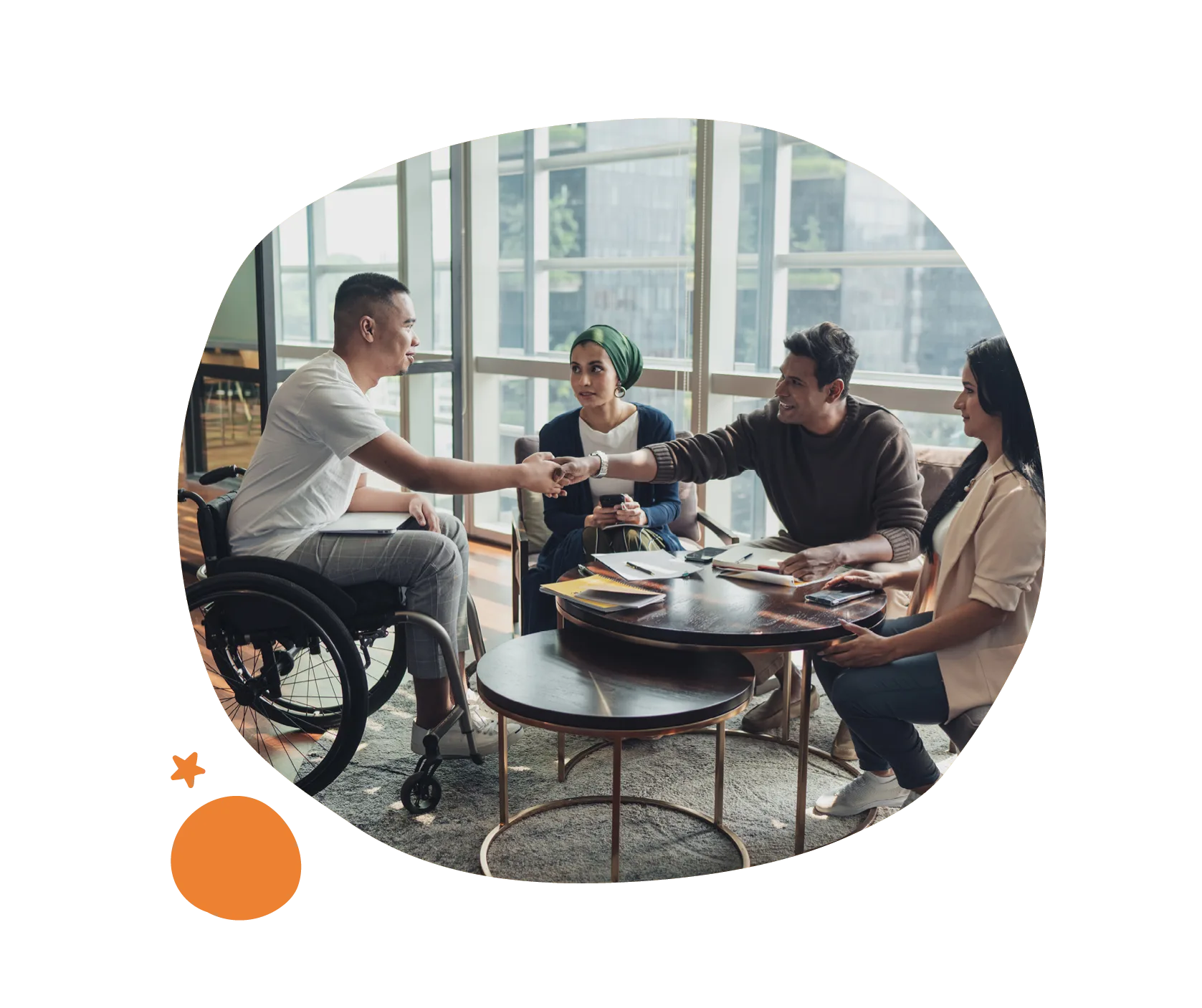 diverse group teamwork, man in wheelchair shaking hands with three colleagues at round table in bright office setting