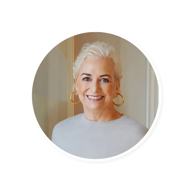 smiling woman with short, wavy white hair and gold hoop earrings wearing a light sweater in a softly lit room, portrait of a confident woman showcasing a warm smile and stylish accessories