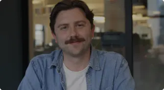 man with a mustache in a light blue denim jacket, modern office setting with blurred background elements