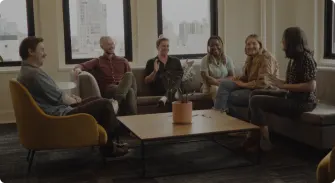 casual group discussion in modern office overlooking city, diverse team sitting on sofas with plants and natural light