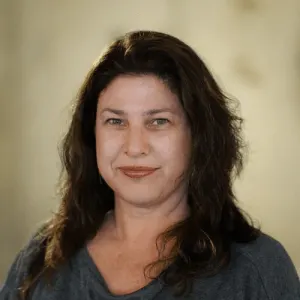 portrait of a woman with long dark hair smiling softly, neutral background emphasizing facial features and soft lighting