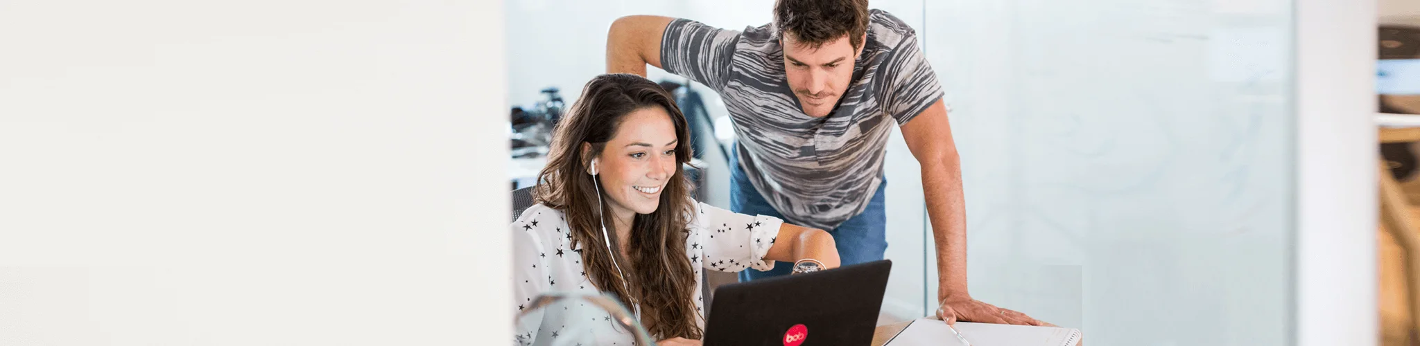working professionals collaborating, woman smiling at laptop with man assisting in a modern office environment
