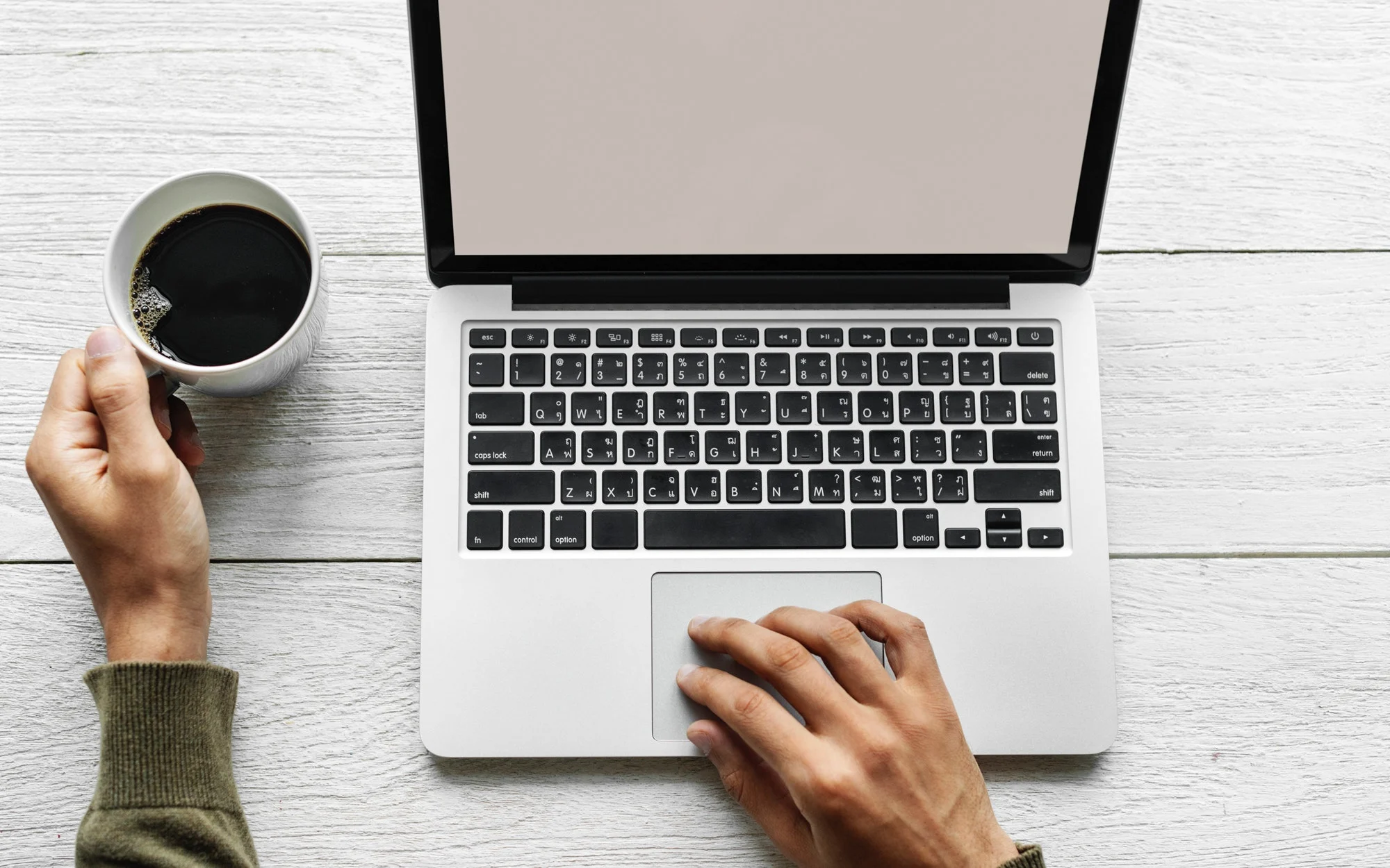 laptop with black keyboard and blank screen beside a hand holding a coffee cup on a wooden table, working with coffee or tea on desk