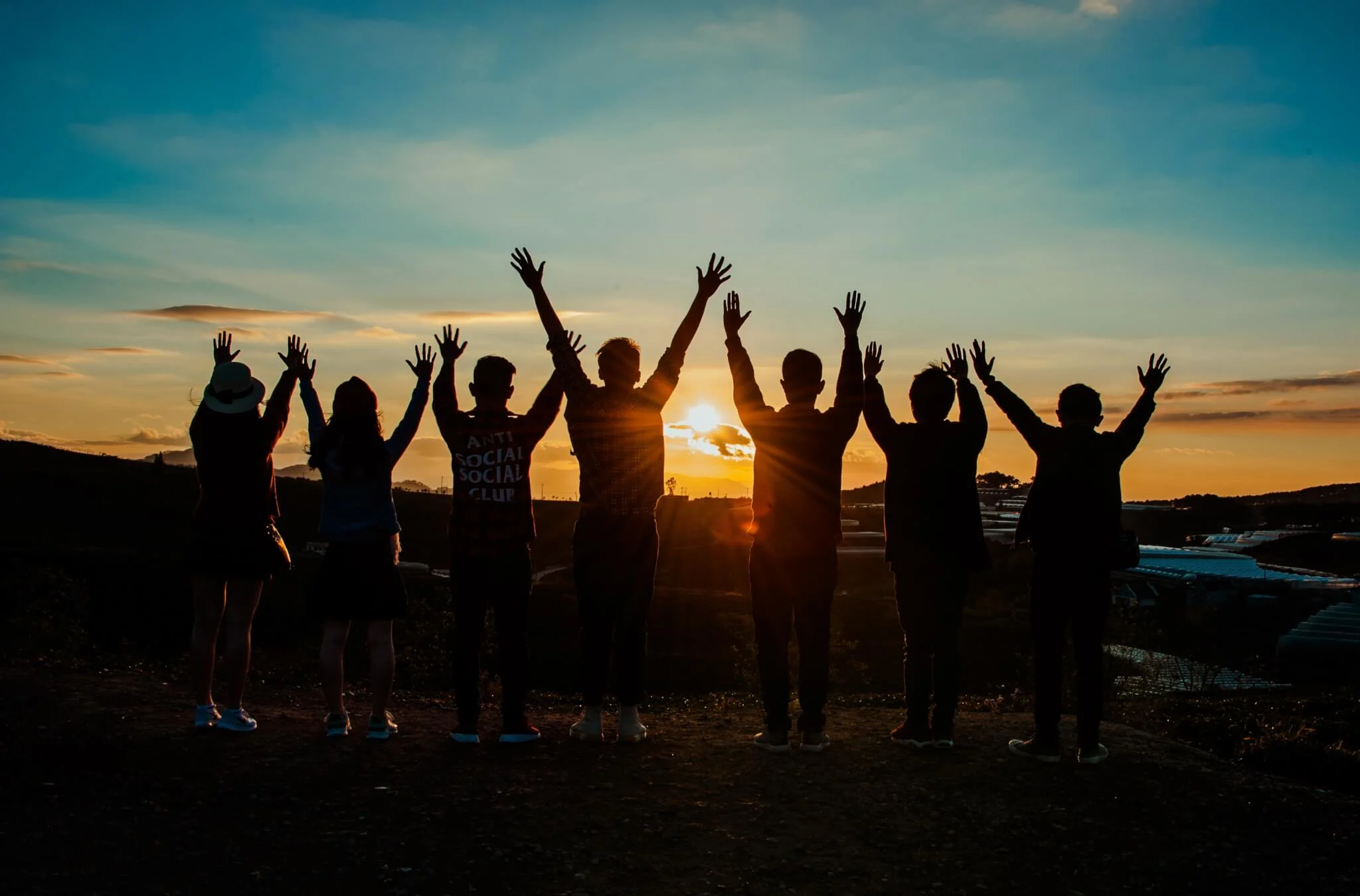 sunset silhouette of friends with raised hands, group celebration against colorful sky background
