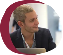professional man in a blazer, engaged in conversation, seated at a desk with a laptop, businessman in profile, modern workspace setting