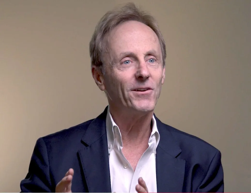smiling man in dark blazer speaking animatedly against a plain background, business professional engaged in conversation