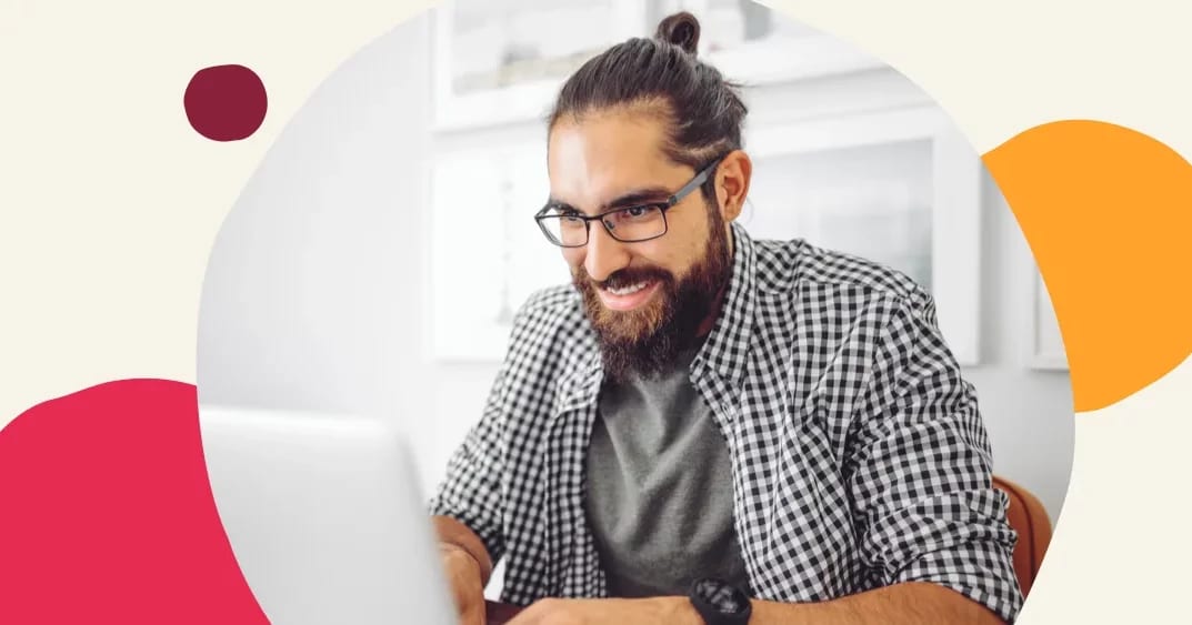 man wearing glasses and checkered shirt working on laptop with a smile, bright office background with abstract design elements