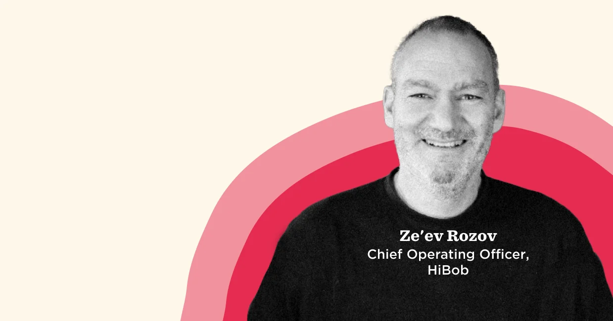 Ze'ev Rozov, COO of HiBob, smiling portrait with vibrant background elements in red and pink tones. Professional setting., Ze'ev Rozov, COO HiBob