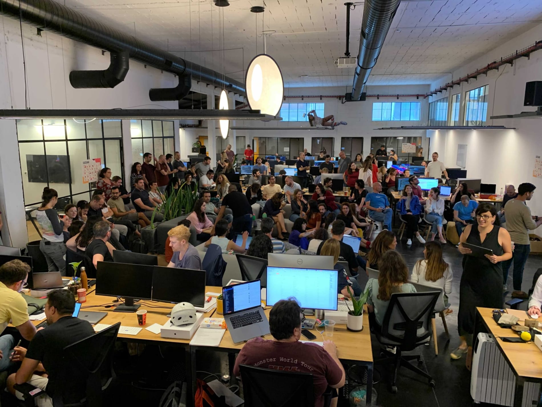 office gathering, diverse group of people collaborating in an open workspace with computers and plants
