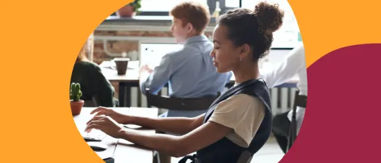 young woman typing at a desk in a modern workspace with colleagues, focused work environment with plants and tech devices