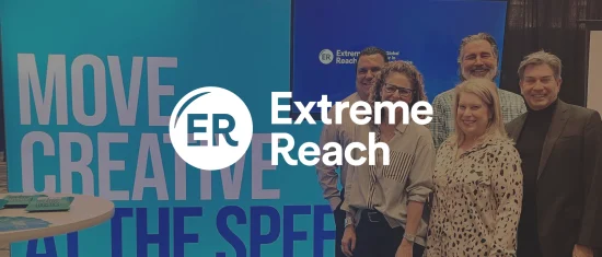 Extreme Reach team at event, showcasing branding with blue backdrop and creative slogan on display. Team smiles together. Extreme Reach, Team Event