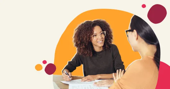 smiling woman with curly hair discussing documents, two women collaborating at a table with vibrant background elements