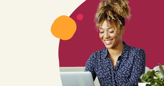 smiling woman in a blue patterned shirt working on a laptop with a green plant and colorful background, happy woman engaged in technology