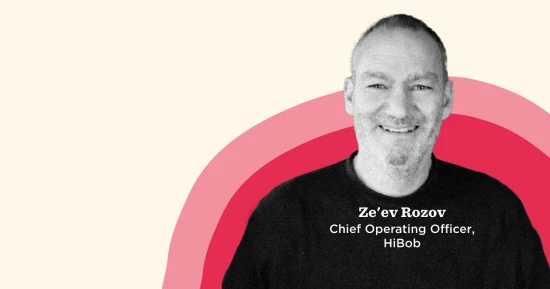 Ze'ev Rozov, COO of HiBob, smiling portrait with vibrant background elements in red and pink tones. Professional setting., Ze'ev Rozov, COO HiBob