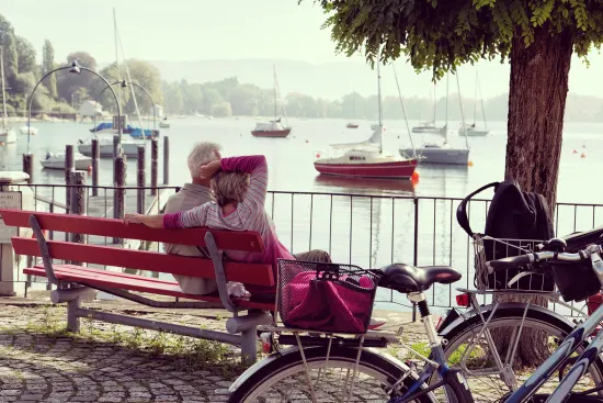 couple sitting on a bench overlooking a serene lake with boats, bikes parked nearby amidst a peaceful, natural setting
