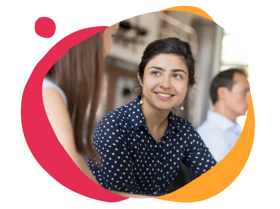 smiling woman in polka dot shirt engaged in conversation, casual work environment with a blurred colleague in background