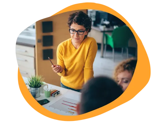 woman in yellow sweater explaining charts, creative meeting setting with plants and stationery on the table