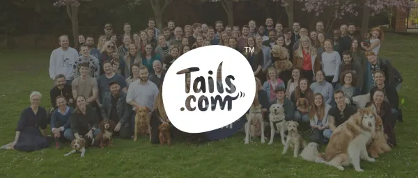 team photo with Tails.com logo, diverse group of people and dogs in a park setting, vibrant greenery and spring blooms, Tails.com team gathering, joyful atmosphere with people and pets in a sunny park