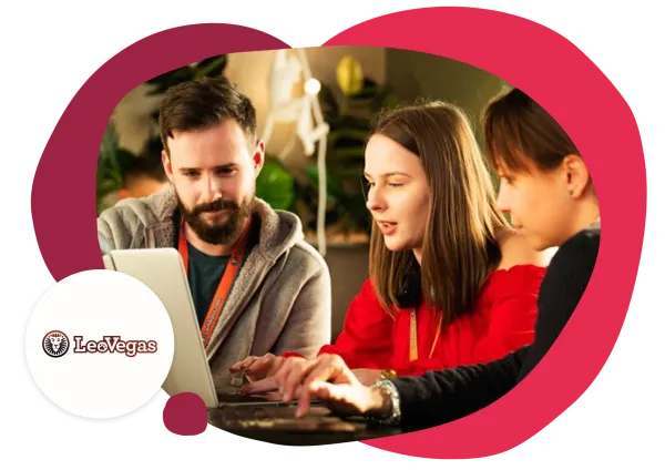 three professionals collaborating on a laptop, discussing ideas in a modern workspace, LeoVegas branding on logo