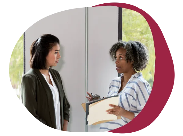 professional women discussing ideas in an office setting with a clipboard and natural light, diverse conversation with a clipboard