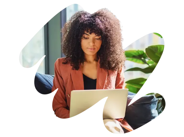 woman working on laptop at home with plants and natural light, curly hair professional in cozy workspace setting