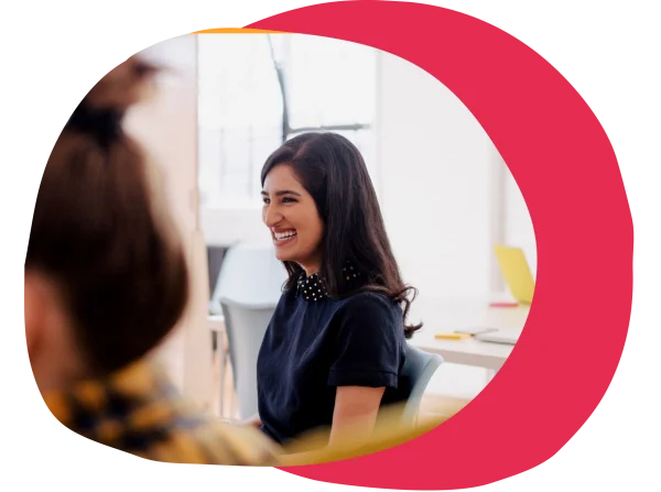 smiling woman in a navy shirt with polka dot collar, engaged in conversation, bright office environment, diverse group discussion in modern workspace
