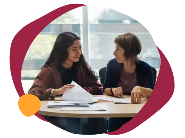 collaborative discussion between two women at a table, sharing documents in a bright, modern workspace, students discussing academic materials