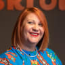 smiling woman with vibrant red hair and colorful floral dress against a blurred background, cheerful expression and stylish outfit